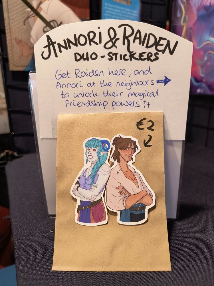 A small display on my artist alley table showing two stickers of Annori and Raiden that fit together back to back. 