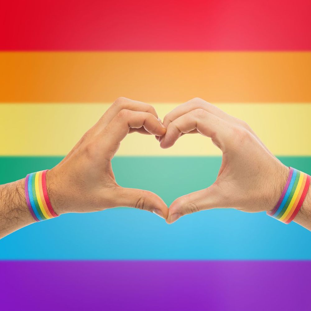 Pride rainbow logo with hands making a heart shape. 