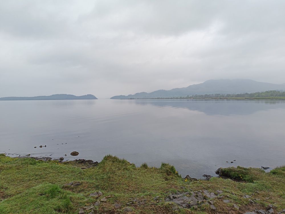 Grey and damp view of Loch Lomond with hills and low cloud in the background