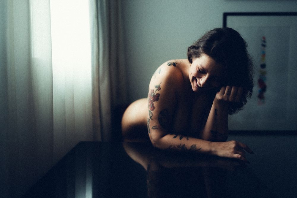 Nu artistique. Modèle féminin nu souriant à côté d'une fenêtre dans une chambre d'hôtel.
