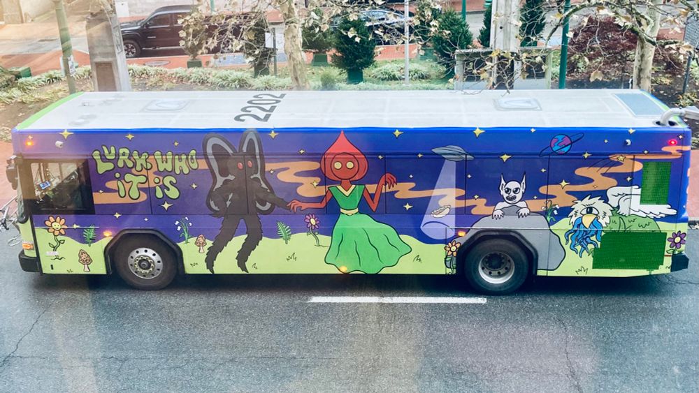 Brightly colored city bus is decorated with illustrations of West Virginia cryptids Mothman, the Flatwoods Monster, Bat Boy and the Grafton County Monster in a field where a flying saucer is landing. Stylized text reads, “Lurk who it is.”