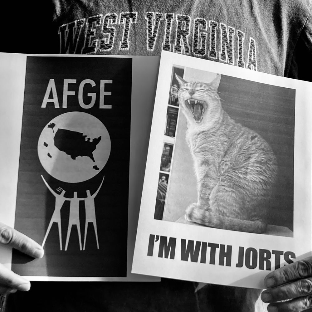 Person wearing a West Virginia t-shirt holds flyers for American Federation of Government Employees and Jorts the Cat.