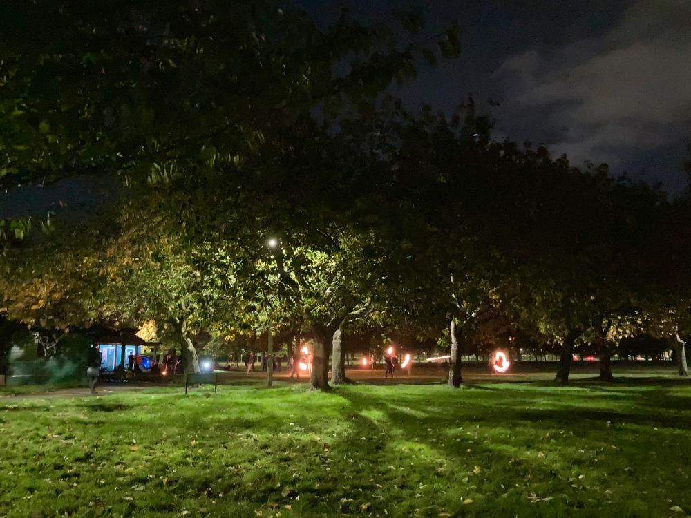 fire twirlers practicing under the trees at night 