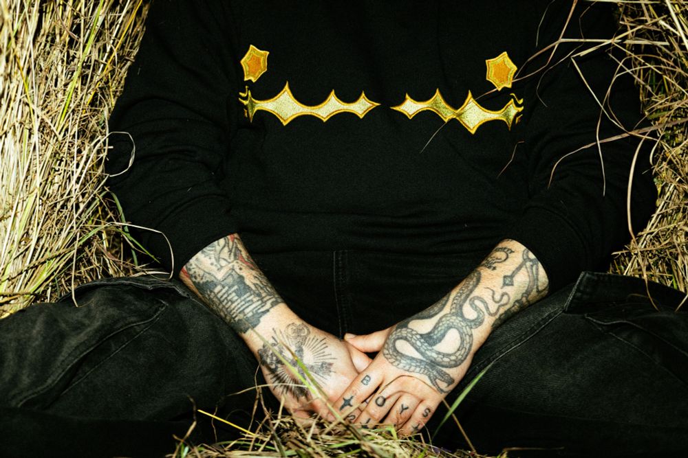 photo of a tattoed man wearing a sweatshirt mimicking the top surgery scars but with star shapes
