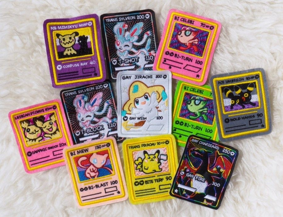 An array of patches in the shape is Pokemon cards including, NB Mimikyu, trans Sylveon, bi celebi, trans Pikachu, gay Charizard 