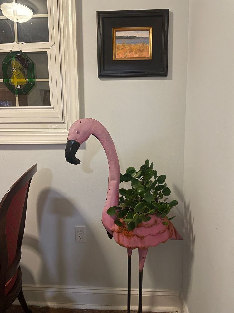 A metal painted life size flamingo statue with a leafy plant inside 
