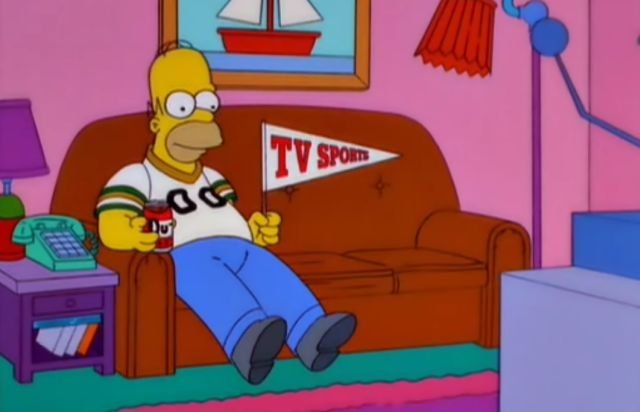 Homer Simpson sitting on the couch watching TV. He's holding a flag that says 'TV Sports'