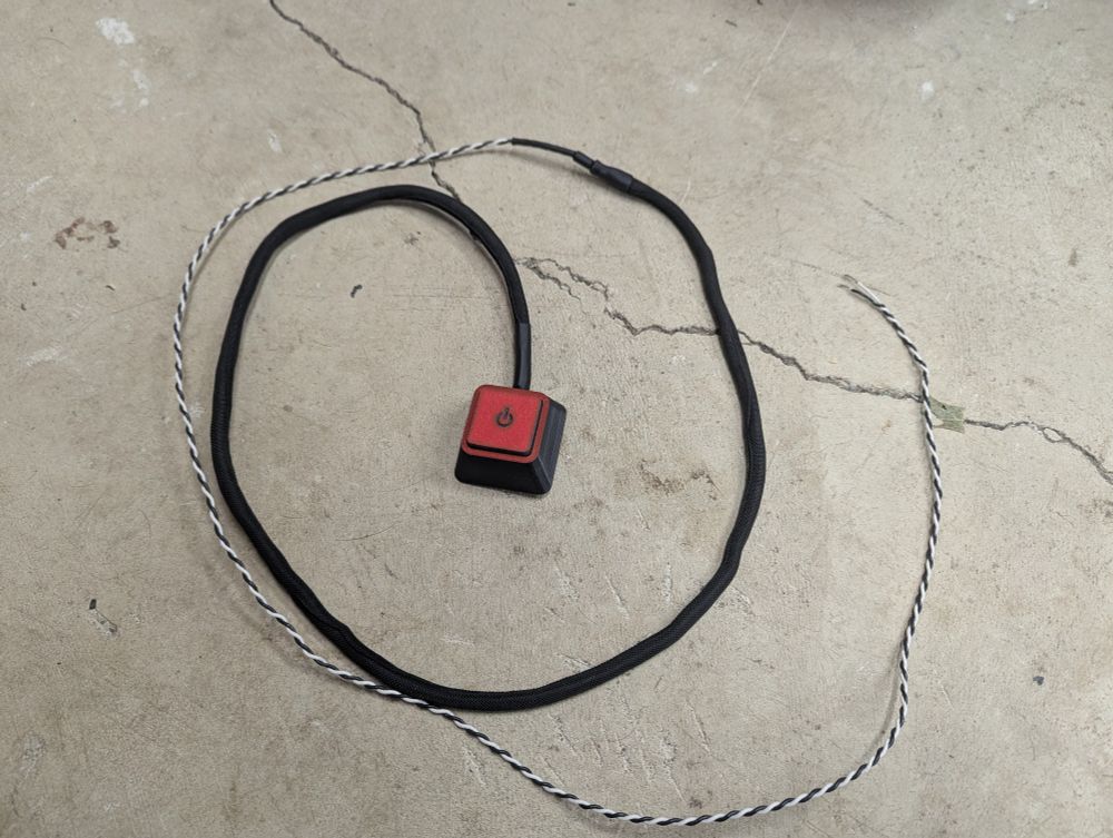 The finished remote power button assembly, black with red accents, with a nylon wrapped cable. 