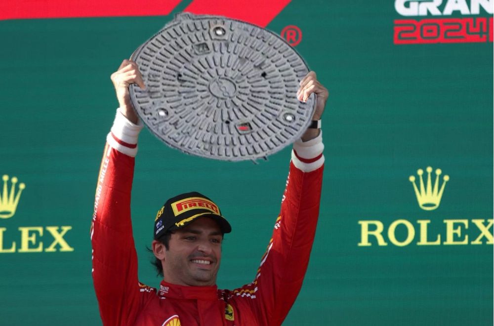 Montaje: Carlos Sainz levanta en el podio una tapa de alcantarilla.