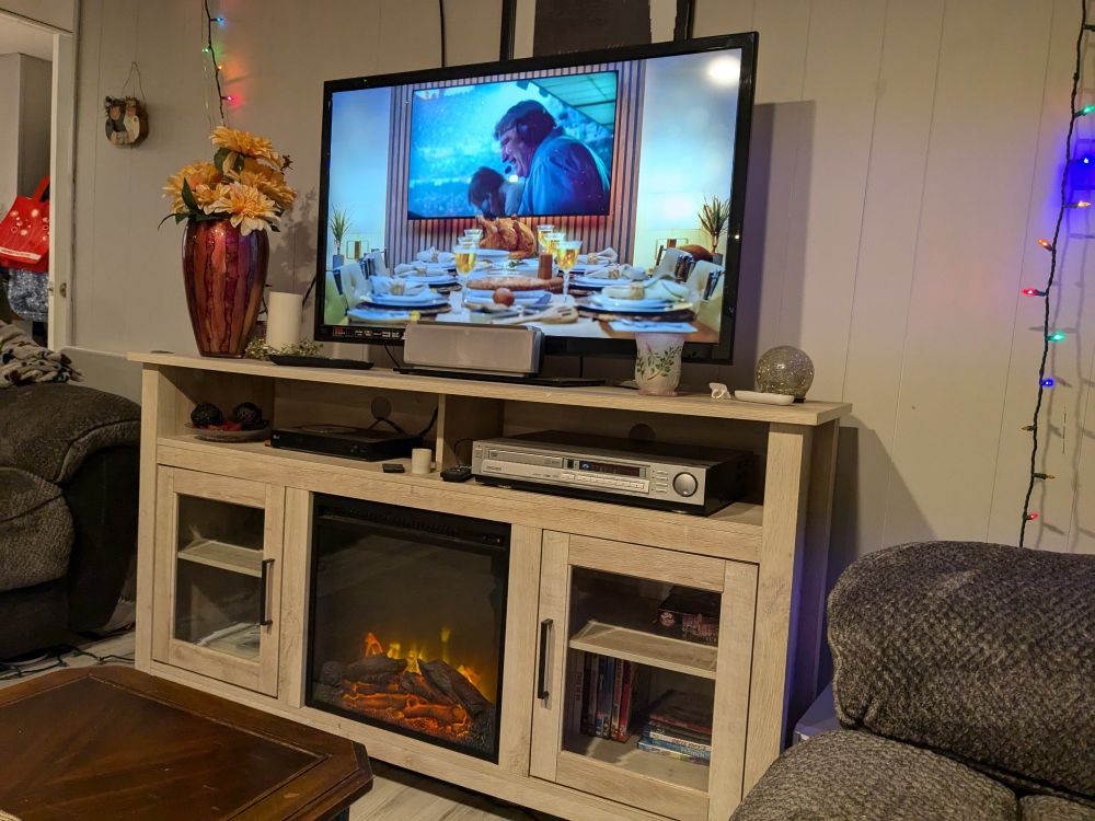 A TV with the Lions Thanksgiving game on it with a fireplace and furniture surrounding it 