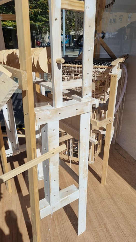 wooden loom sculptural work that is also a city with tiny people in it