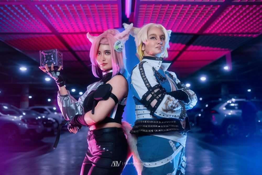 Wicked Thunder cosplay holding up an electrode cube back to back with a Retsarra cosplayer with crossed arms