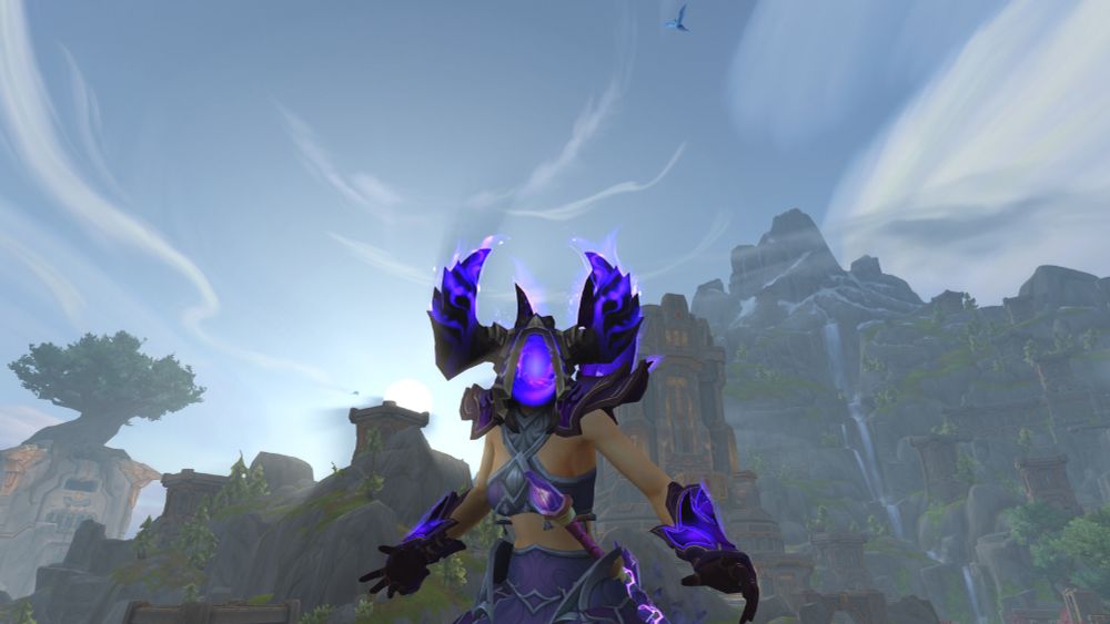 My World of Warcraft Warlock. She has a helmet on with glowing void horns and a spiralling void where her face should be. She has purple shoulders and gloves and a revealing two part dress on. Behind her is the dawning sunlight breaking through the mountains of the Isle of Dorn.