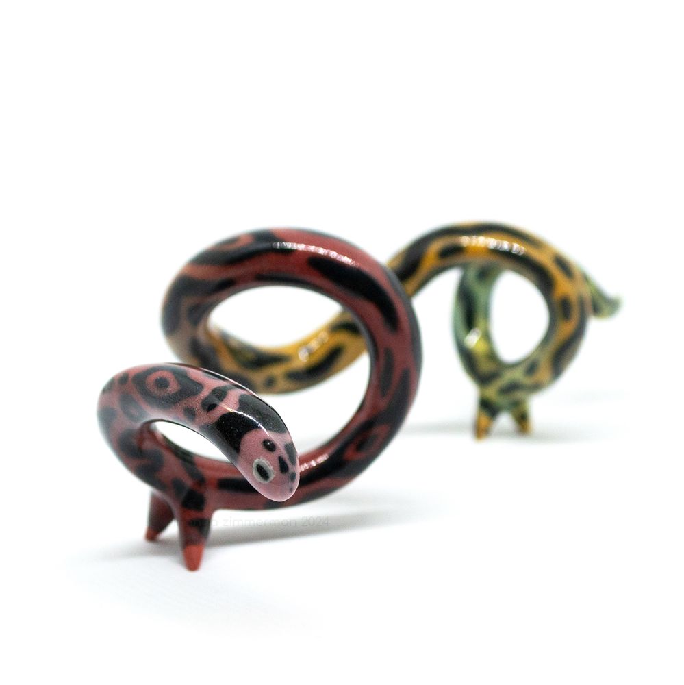 A long and spindly ceramic salamander-snake with multiple loops.  The body is gradient from red to yellow, with patterns reminiscent of a dart frog. The glaze is glossy.