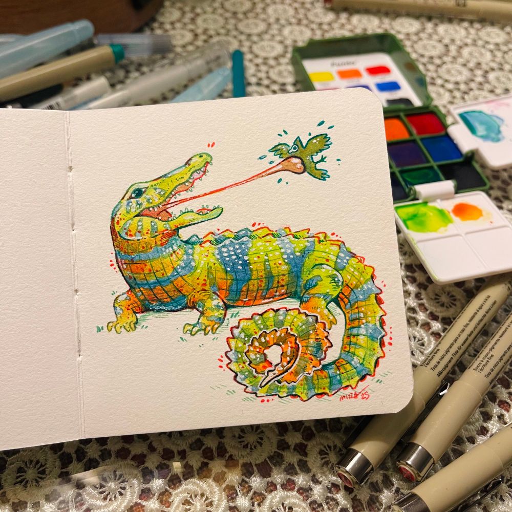 A watercolor, ink, and colored pencil illustration of an alligator/chameleon hybrid in a small square watercolor-paper book.  The form is an alligator, with the coloration, tongue, and swirly tail of a panther chameleon.  It’s using its tongue to catch a bird snack!