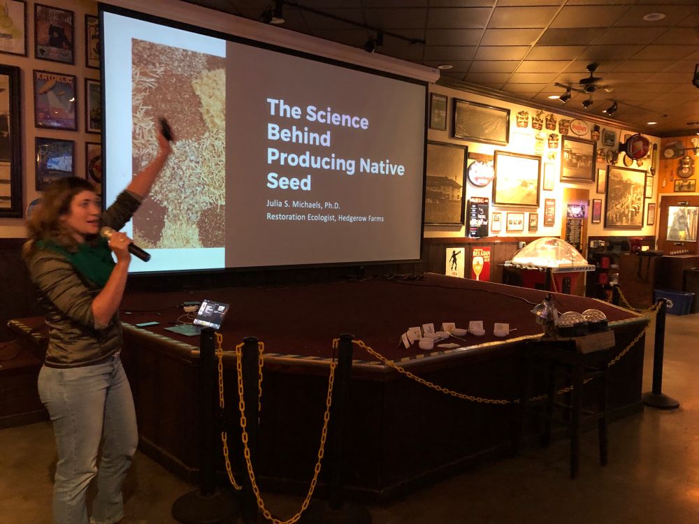 Photo of Julia Michaels at a bar stage with screen title The Science Behind Producing Native Plant Seed