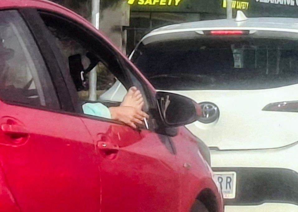 Guy driving with both a foot and a hand holding  a cigarette stucking out of the driver's open window.