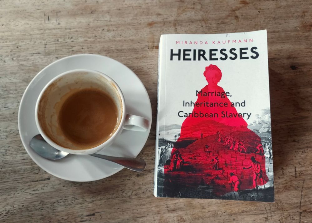 A copy of the book "Heiresses: Marriage, Inheritance, and Slavery in the Caribbean" by Miranda Kaufman, next to a coffee cup. 