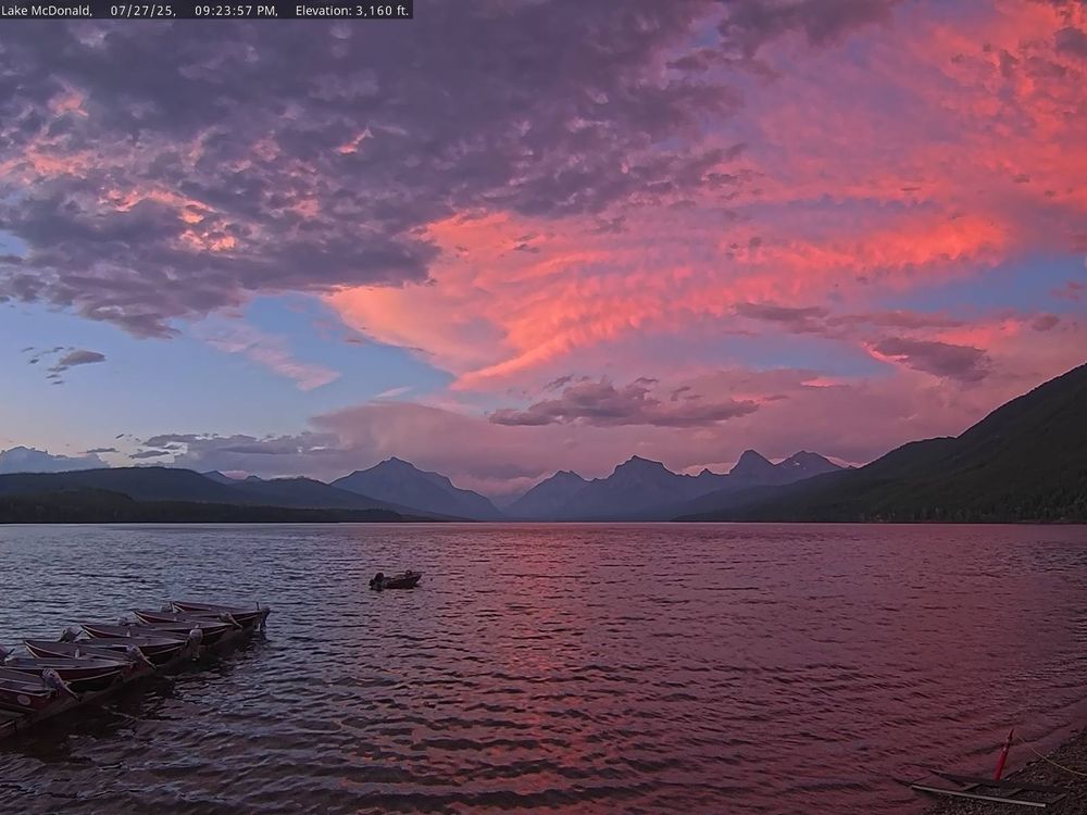 Dramatic sunset skies and mountains of red, peach, blue, and purple over Lake McDonald in Glacier National Park