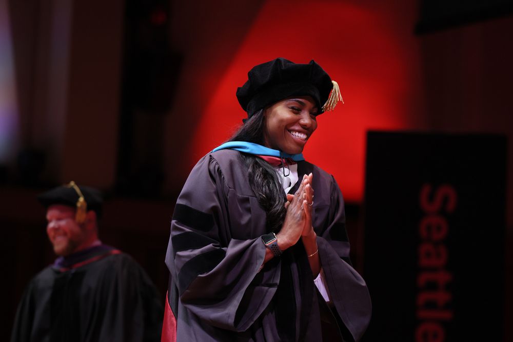 A student wearing regalia claps their hands together.