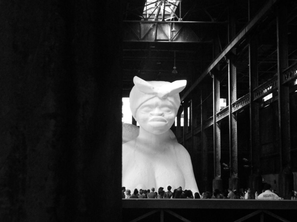 White sugar based statue of a Black woman. Naked, crouched in the Sphinx position.