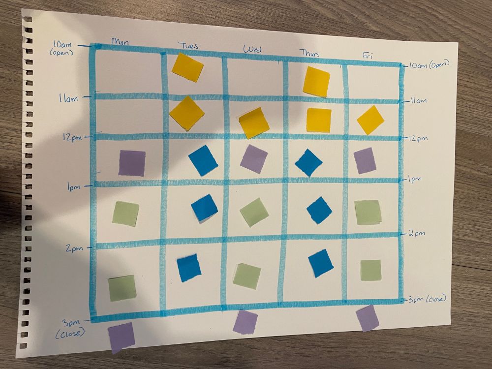 White paper with a weekly schedule in blue divided into one-hour time blocks from 10am to 3pm. Gold, purple, blue, and green paper squares fill the time blocks on the page.
