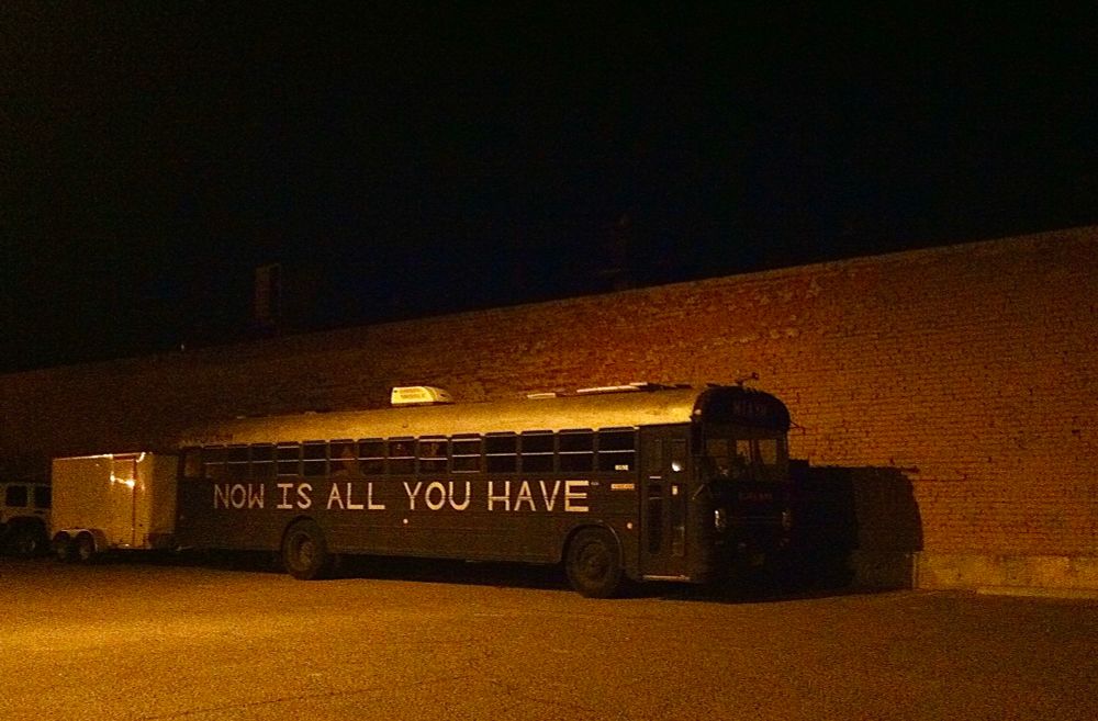 Old lone bus in the dark, with words “now is all you have” painted on side