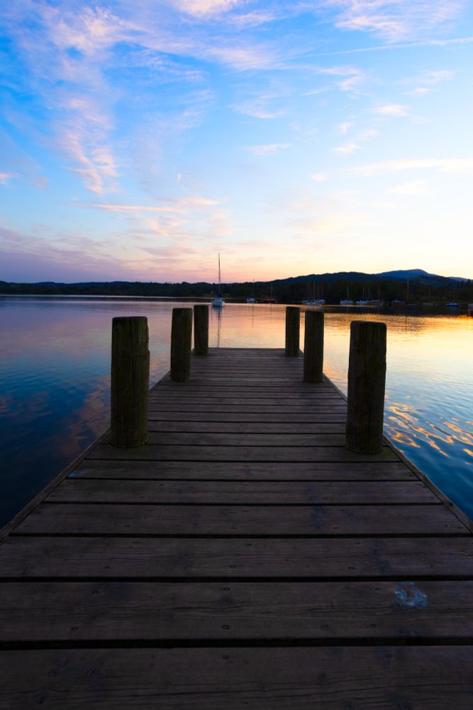 A pier reaching into a lake with a blue and pink sunset reflecting on Windermere, Cumbria