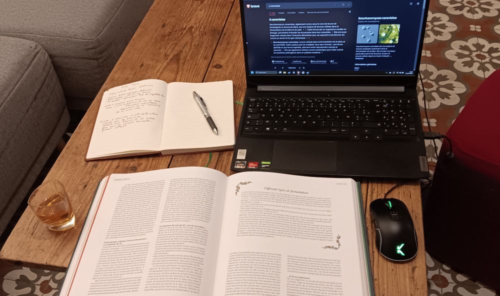 Une photo montrant une table avec un ouvrage sur l'oenologie, un carnet de notes, un ordinateur portable pour effectuer des recherches et un verre d'armagnac, bien sûr!