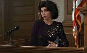 Marisa Tomei as Mona Lisa Vito in My Cousin Vinny, on the stand in the courtroom wearing a purple dress with shiny appliquéd gems, looking annoyed/insulted