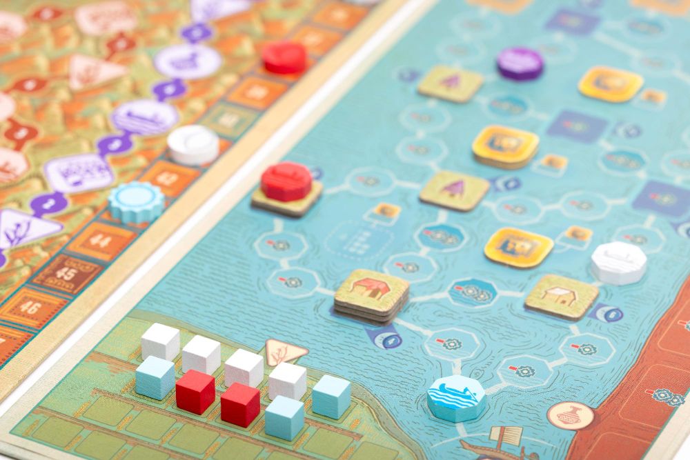 A close-up photo of a side board alongside the main game board in Ayar, depicting a lake with various cardboard tokens and coloured wooden pieces placed around it.