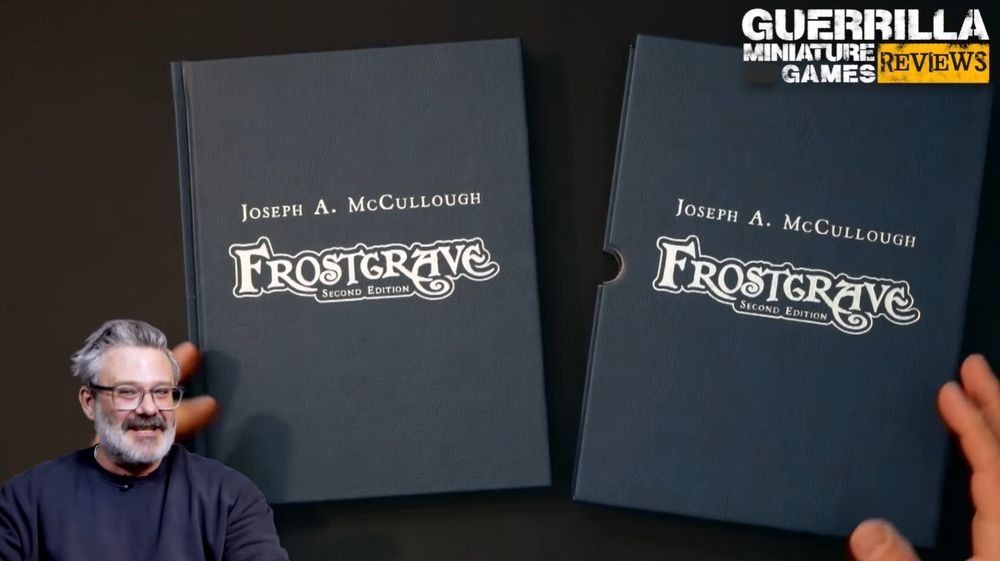 A screengrab from the Guerrilla Miniature Games YouTube flipthrough of Frostgrave: Second Edition special edition, showing host Ash Barker alongside the faux leather, silver-foiled book next to its matching slipcase.