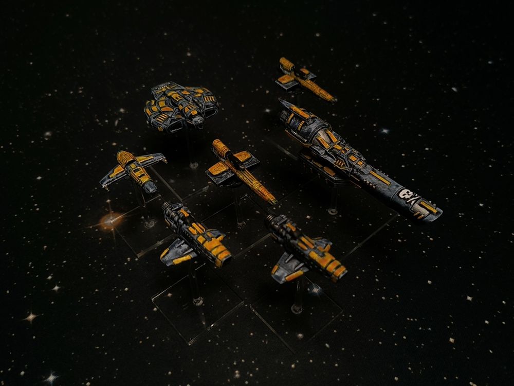 A photo of fully painted miniature figures of spacecraft for the wargame Voidfighter: a range of fighters and larger ships with a matching yellow paint scheme, against the black and stars of space.