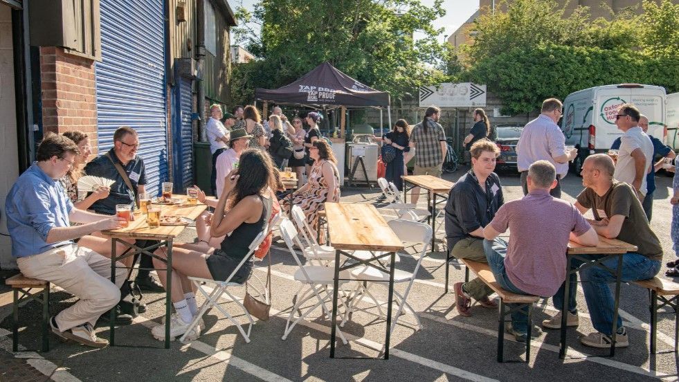 A photo of lots of people sat and stood around in the sun outside the Tap Social Movement Oxford.