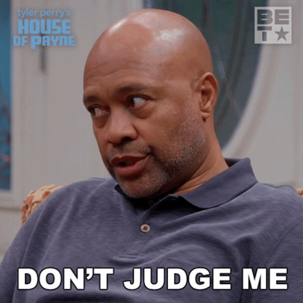 a bald man with a beard is sitting in a chair and says " don 't judge me "