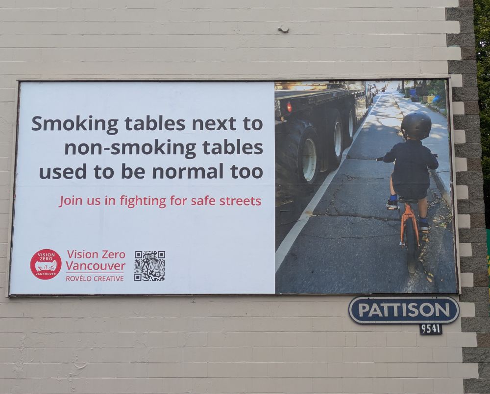 Billboard reads: Smoking tables next to non-smoking tables used to be normal too. Join us in fighting for safe streets. The vision Zero logo and Rovelo Creative are listed below. On the right, a photo of a young child riding a bike on the shoulder of a road next to a very large truck.