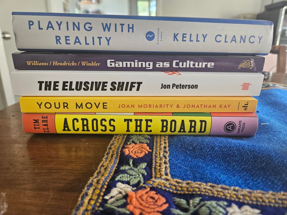 A stack of books about games including playing with reality by Kelly Clancy, gaming as culture by Williams Hendricks and Winkler, the elusive shift by Jon Peterson, your move hy Joan Moriarty and Jonathan Kay and across the board by Tim Clare. 