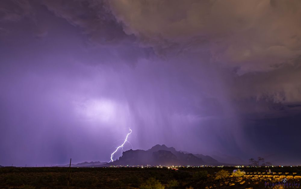 A bolt of lightning illuminates Superstition Mountain on the Eastern edge of the metro Phoenix, AZ area. Brilliant purples backlight the shafts of rain and illustrate the surface level wind generated by the storm moving left-to-right in this frame.

Photo credit:
Brian Blakesley Photography