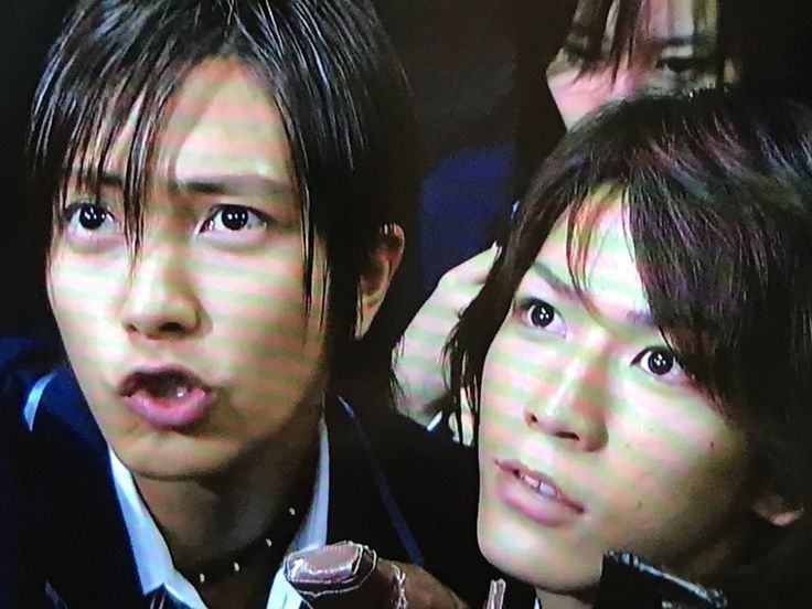 photo of japanese high + school drama 『 nobuta wa produce 』 scene with the aliasing television filter ， akira is in the middle of talking & pronouncing a sh should really strongly with shunji right next to him  staring up at whoever akira is talking to with his front teeth peeking out of his lip ， nobuta is behind them gripping her back + pack strap & keeping her eyes low ， shunji is holding up something that is cropped but appears made of leather & another rectangular object