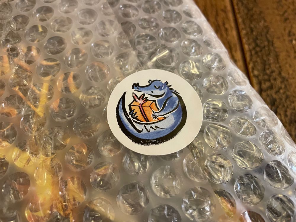 A close-up of the sticker sealing the wrapping shut, showing a dragon holding a gift box.