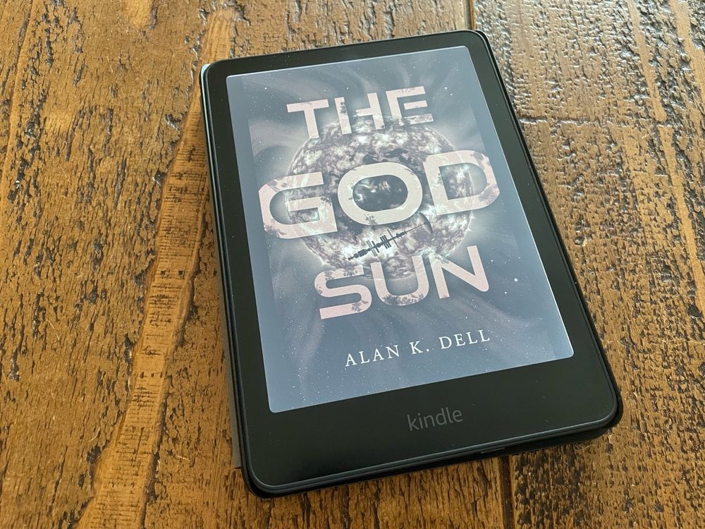 A Kindle placed on a table, showing the cover artwork for “The God Sun” by Alan K. Dell.