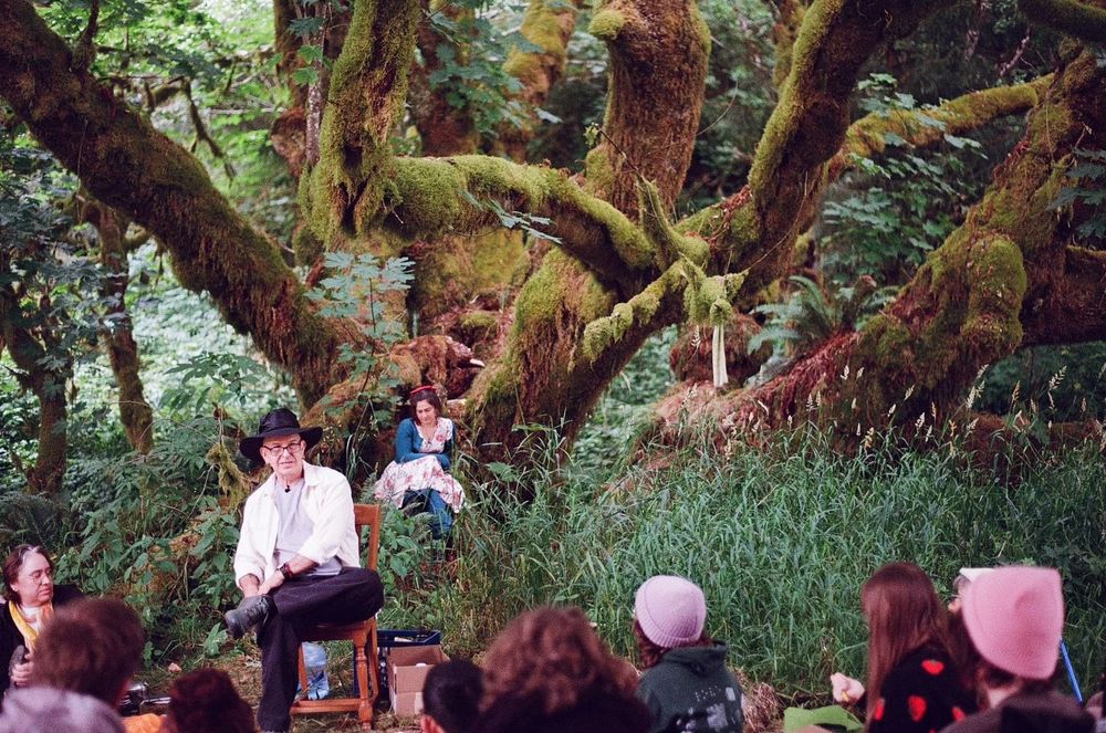 Aidan Wachter sits beneath a huge moss-covered maple tree, talking to people seated nearby. 