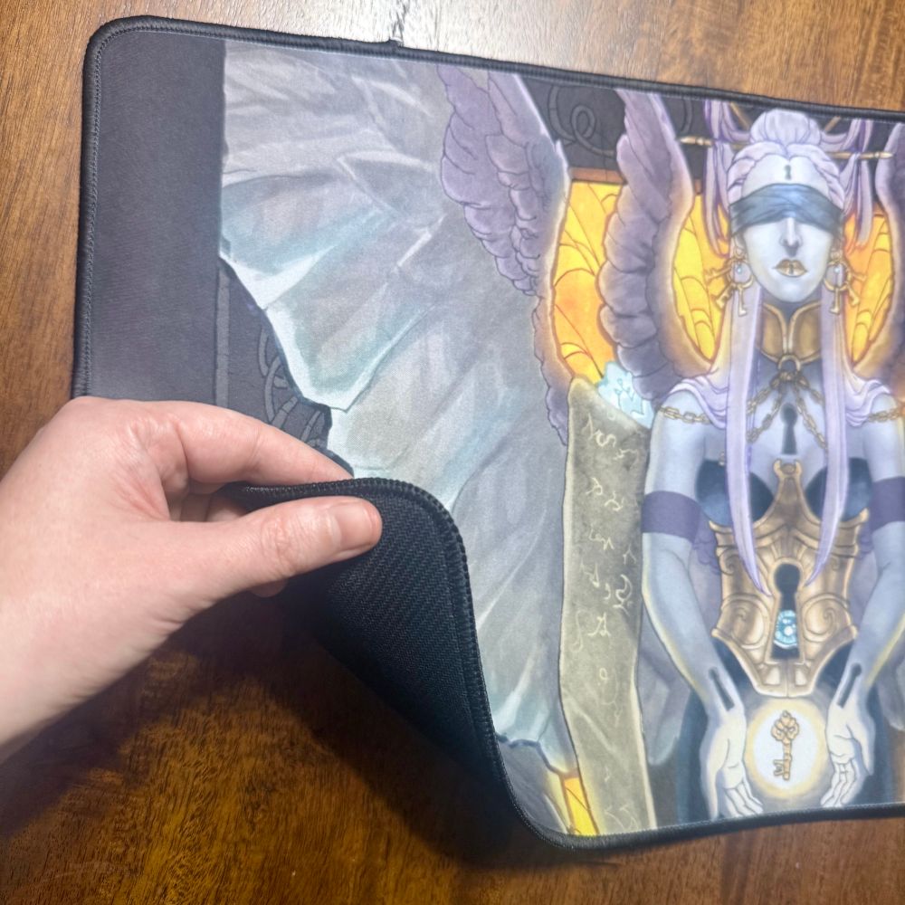 Desk mat with stitched edge featuring an illustrated design of a blind angel.  Nice printing and the stitching is luxurious, though I may up the vibrancy and highlights in my art before printing next time.