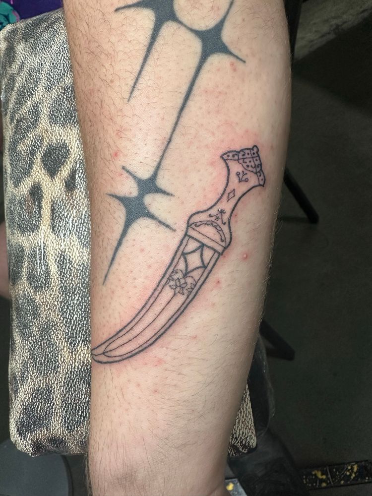A fresh linework tattoo of an intricate dagger.