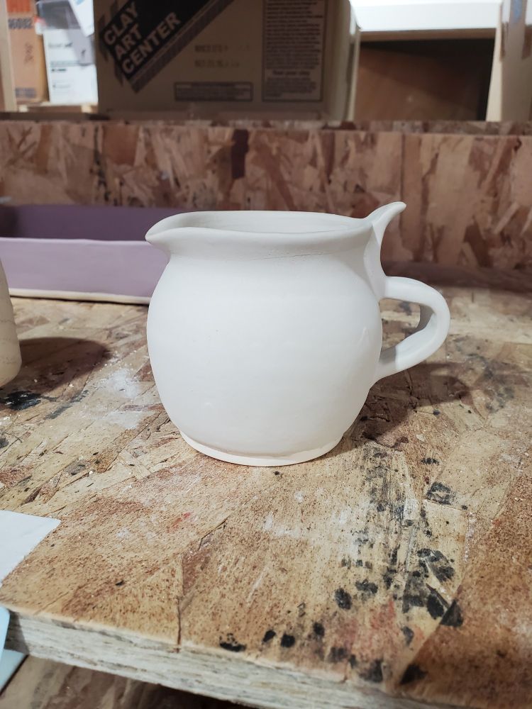 Small ceramic pitcher on a shelf with glaze, pre-final fire in the kiln.