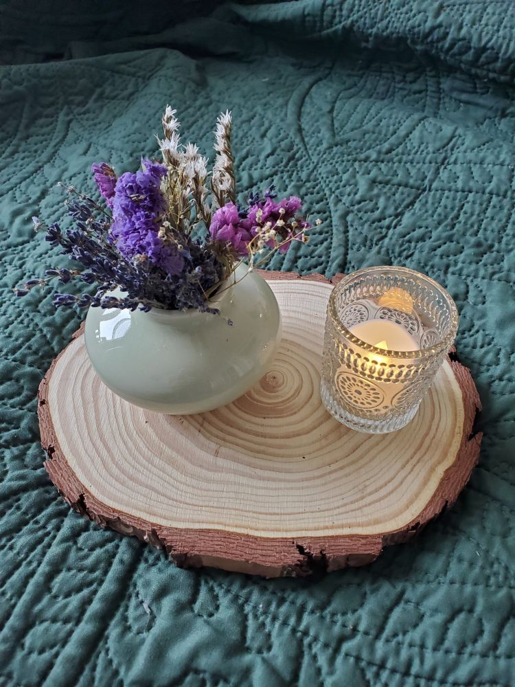 Small green vase with a bouquet of dried lavender, pink, and white flowers sitting on a wood slice. And a faux votive candle. 