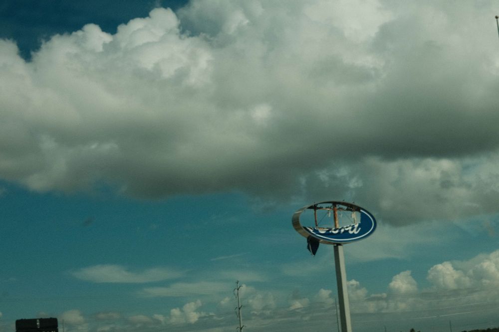 A Ford motor company highway sign, but the center has been ripped  out, by wind or some kind of weather. 