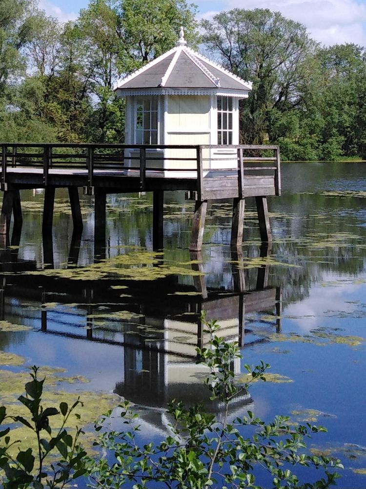 Alter Badesteg  mit Badehäuschen spiegelt sich im glatten See.