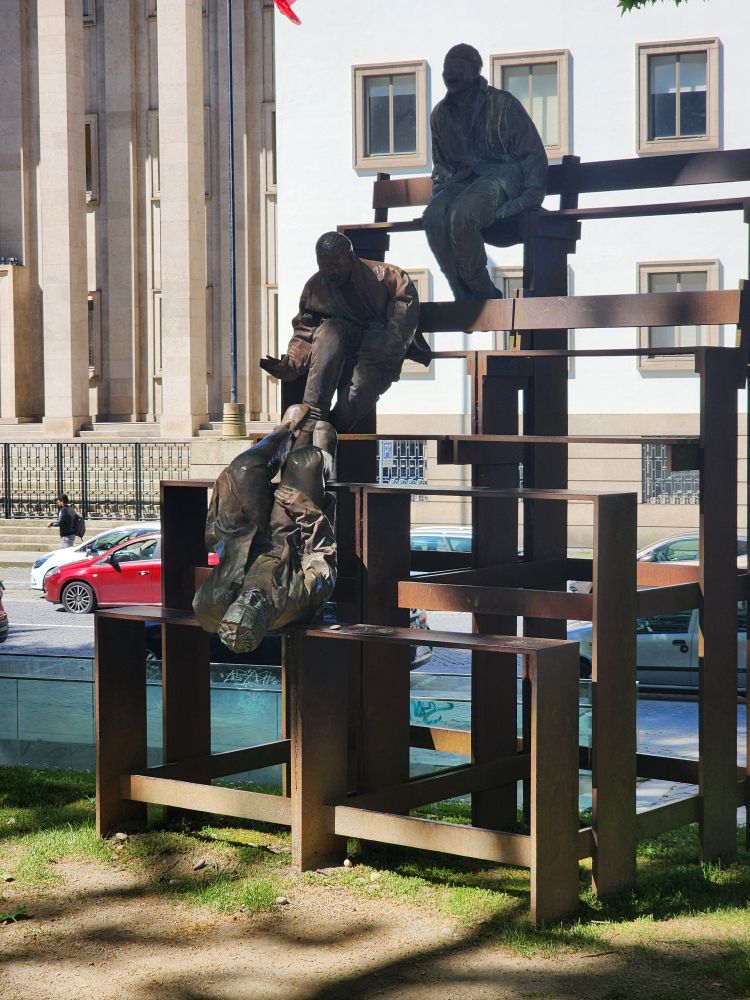 Sculpture of men on bleachers, one of whom is falling.