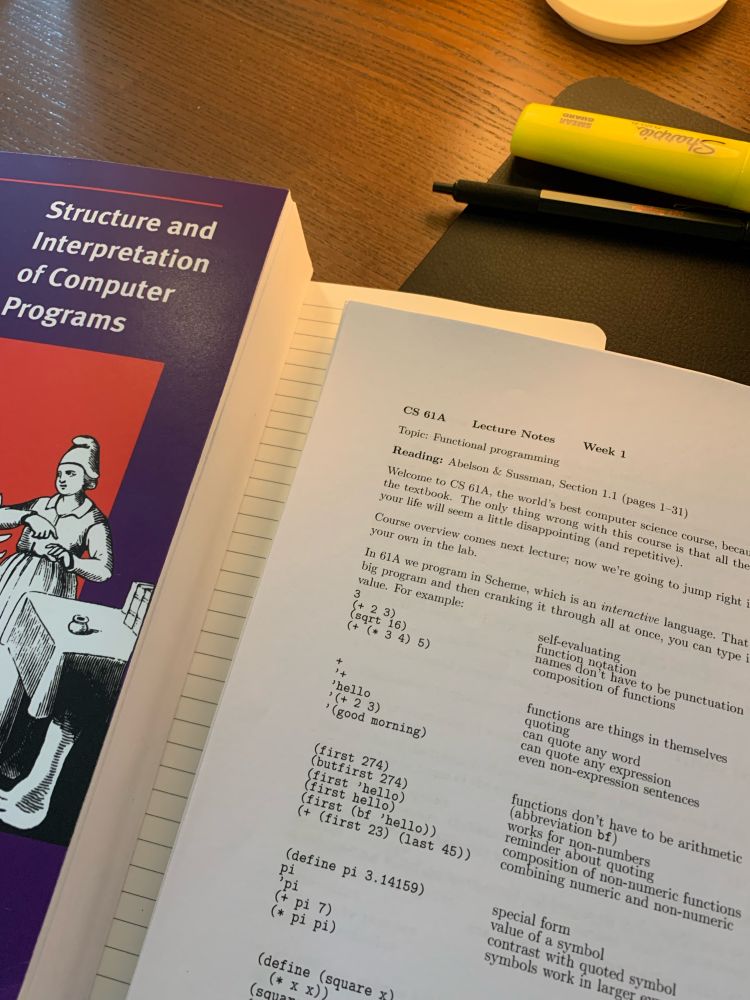 Lying on a desk is a ruled notebook, a printed course packet from Berkeley CS 61A (2010), the Structure and Interpretation of Computer Programs textbook and some pens, lit by a warm desk lamp out of frame. 